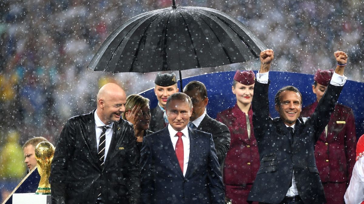 Frankreichs Präsident Emmanuel Macron (r.) freut sich im Regen, Russlands Präsident Wladmir Putin (Mitte) und Uefa-Chef Gianni Infantino haben einen Regenschirm.