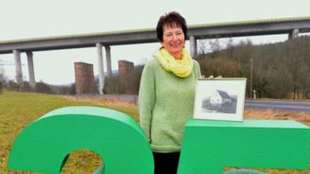 Wilma Bause posiert an der grünen Jubiläums-25 mit einem Foto ihres Wohnhauses. Im Hintergrund sind  die neugebaute und 1995 freigegebene Weihetalbrücke mit den als Denkmal erhaltenen zwei Brückenpfeilern der alten Reichsautobahn Nr. 4  zu sehen. Foto: Hanno  Müller