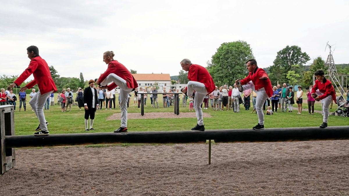 Sportler aus dem Turn- und Gymnastikverein Waltershausen haben die originale Zöglingskleidung angelegt und führen von Johann Christoph Friedrich GutsMuths kreierte Übungen — hier den „Fußkuss“ — auf dem Schwebebalken aus. Matthias Cramer hat sich als GutsMuths gewandet und leitet die Vorführungen an.