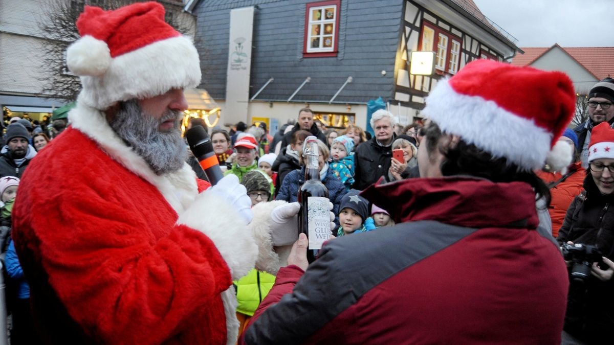 Weihnachtsmann Falk Braun (links) überreicht Ruhlas Bürgermeister Gerald Slotosch eine Flasche Glühwein.