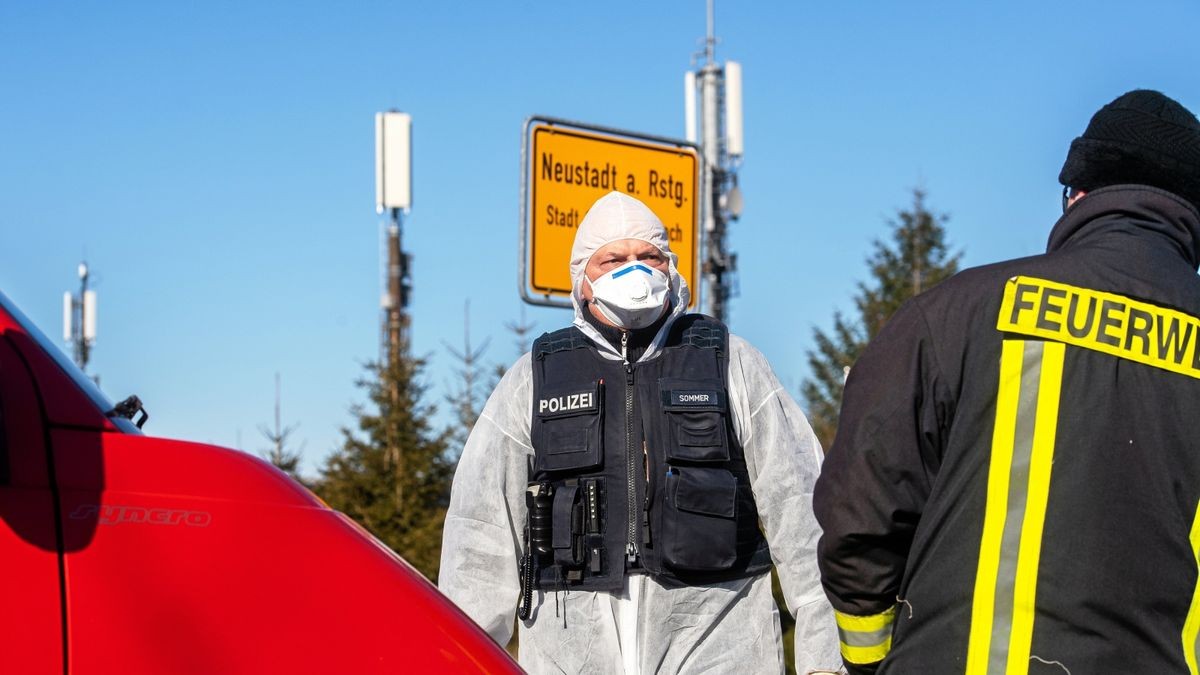 Ein Polizist in Vollschutzanzug sowie Feuerwehrleute am Ortseingang von Neustadt am Rennsteig. Im dem Ort ist die Zahl der Corona-Fälle weiter gestiegen. Der Ort wurde am Sonntag für zwei Wochen komplett unter Quarantäne gestellt.