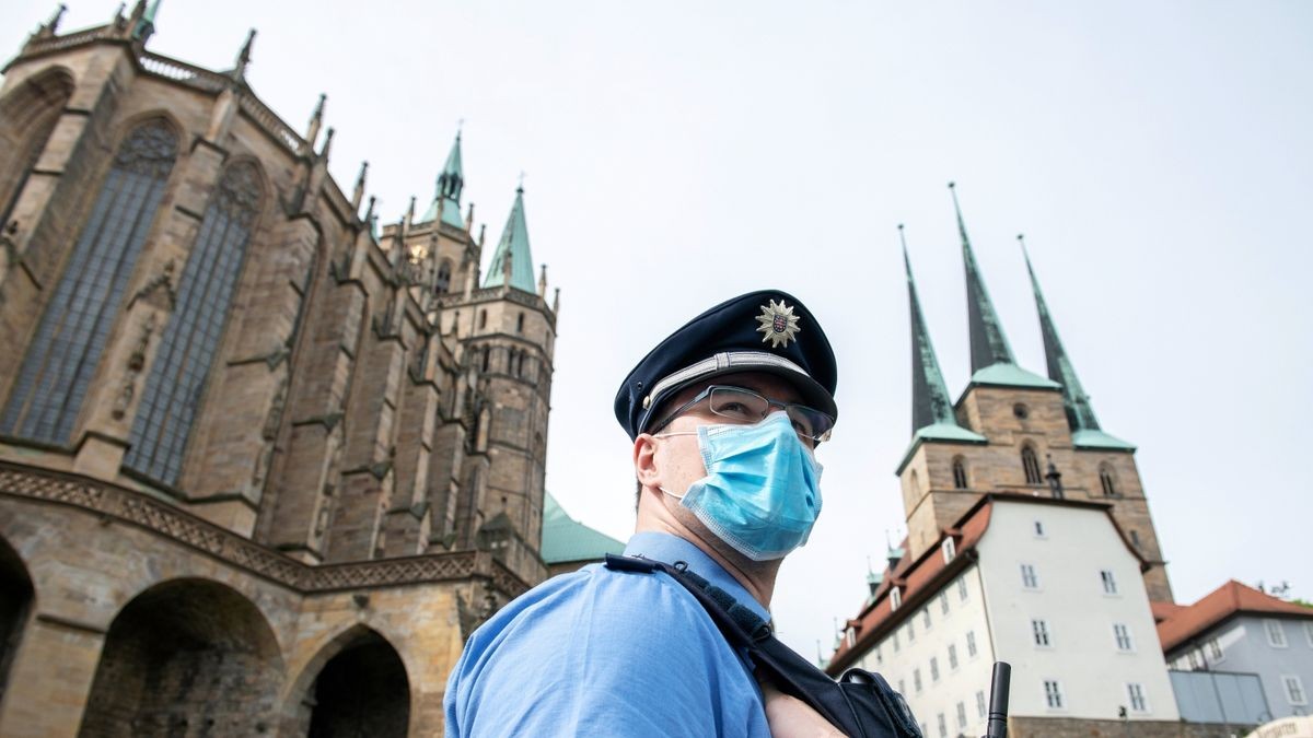 Ein Polizist steht vor dem Dom in Erfurt mit einer Atemschutzmaske.