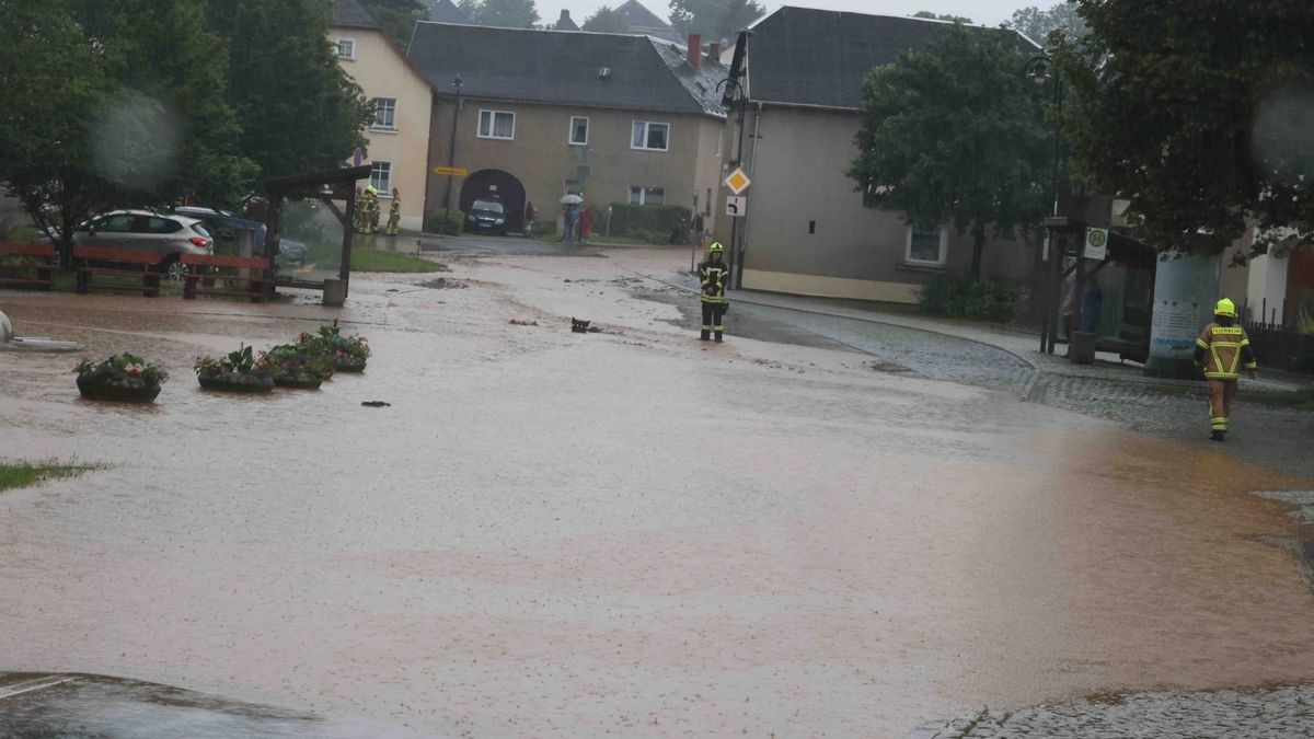 Die Feuerwehr versucht am Freitag, den überfluteten Rathenauplatz in Zeulenroda-Triebes von Unrat zu befreien. Nach einem heftigen Gewitter sind Wasser und Geröll von Feldern in die Stadt geflossen. Auch Anwohner helfen mit.