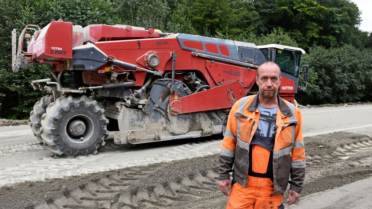 Frank Milz steht vor der Fräse, mit der er das Zementpulver mit dem Sand und Kies des Fahrbahnuntergrundes vermengt.