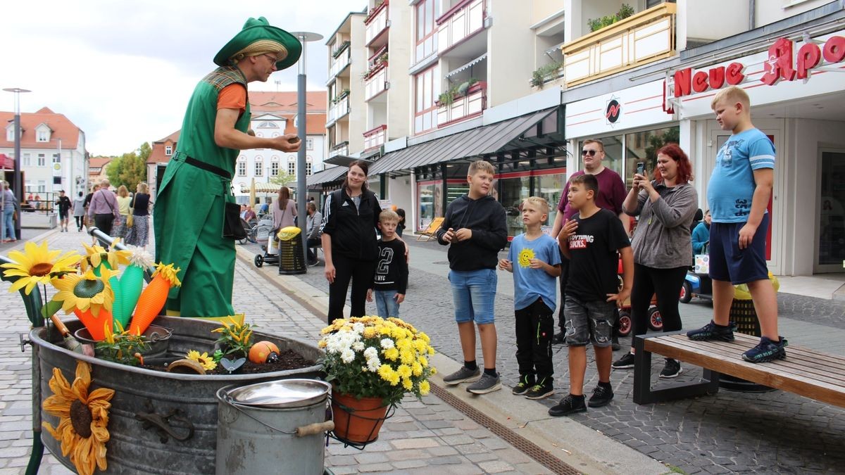 Imanuel Immergrün, ein Gartenwalkact in Übergröße, unterhält die Bauernmarkt-Besucher, so auch Jessica Weigert, Maurice, Julian, Elias, Max, Adrian Unverricht, Angelique Linde und Jonas.