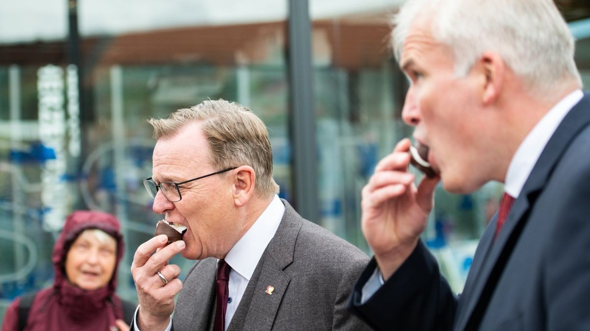 Ministerpräsident Bodo Ramelow (Die Linke) und OB Andreas Bausewein beissen in einen Schokokuss am Stand des Bundeslandes Hessen.