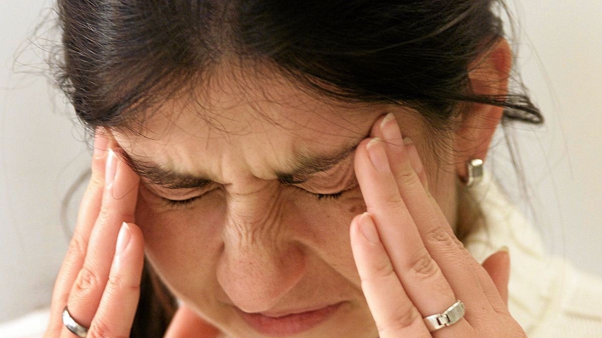 Eine junge Frau hält sich mit schmerzverzerrtem Gesicht ihren Kopf (Symbolfoto) 