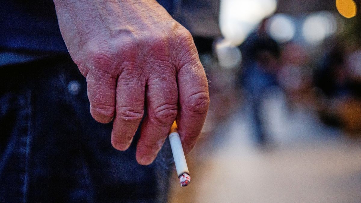 Ein Mann steht auf einer Straße und hält eine brennende Zigarette in der Hand. In der Unterführung am Hauptbahnhof soll ein Appell zum Verzicht auf die Kippe bewegen, damit andere Wartende nicht länger im Rauch stehen. 