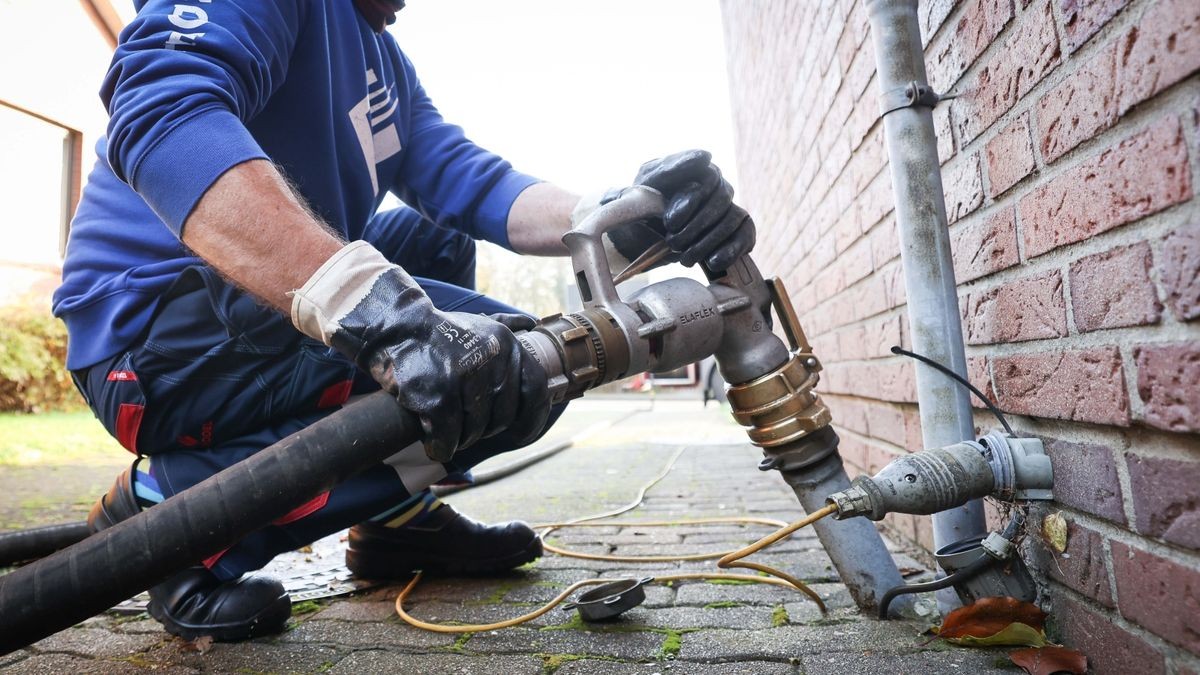 Ein Mitarbeiter eines Diesel- und Heizöl-Unternehmens befestigt die Zapfpistole an einem Füllstutzen für die Heizöllieferung an einen Kunden in einem Einfamilienhaus.