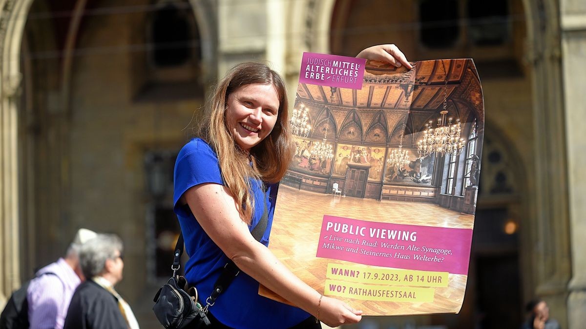 Karina Halbauer von der Kulturdirektion zeigt das Plakat, mit dem die Stadt auf das Public Viewing zur Welterbe-Entscheidung aufmerksam macht.