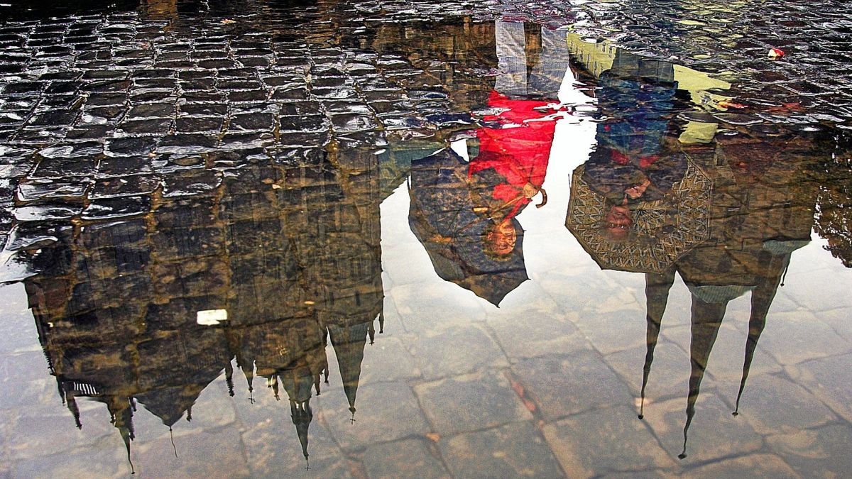 Eine Touristin spiegelt sich in einer Pfütze am Erfurter Domplatz. (Archivbild)