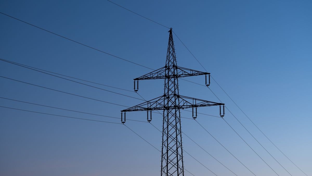 Ein Strommast ist bei Sonnenaufgang als Silhouette zu sehen.