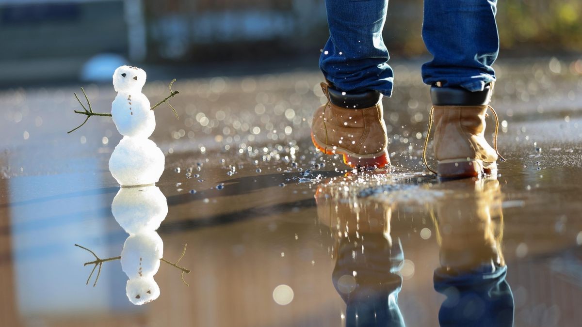 Ein Mann läuft durch eine Pfütze mit Tauwasser, in der ein Schneemann steht.