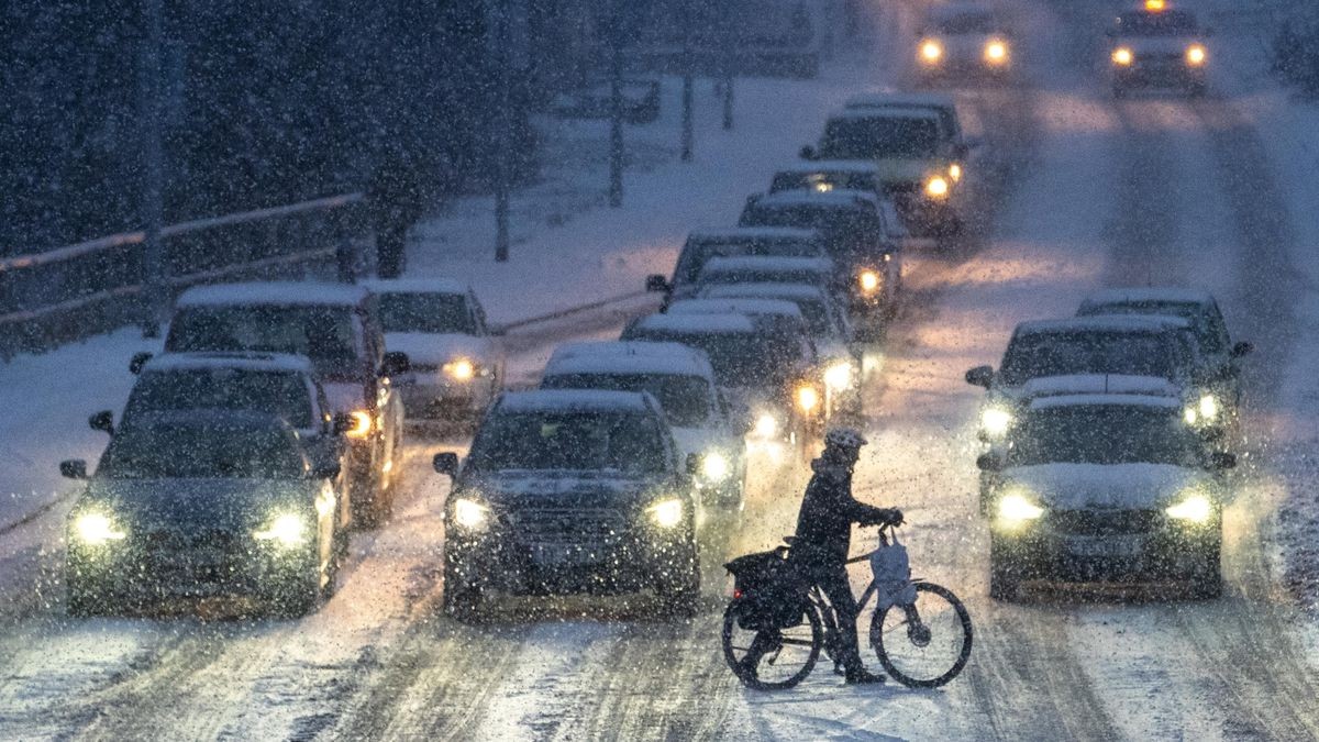 Ein Radfahrer schiebt am späten Nachmittag sein Rad über die verschneite Erfurter Staufenbergallee.