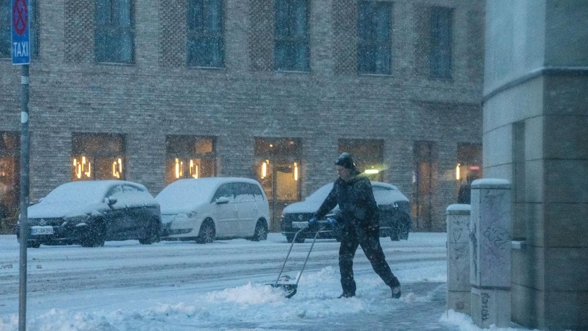 Ein Mann schiebt Schnee von einem Gehweg in der Erfurter Innenstadt.