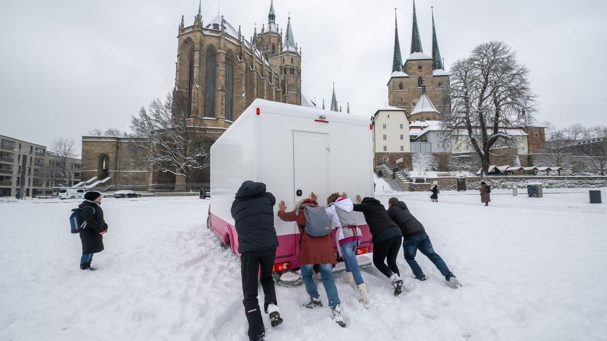 Helfer schieben am Nachmittag das Fahrzeug eines Verkaufsstandes auf dem Domplatz an (im Foto).