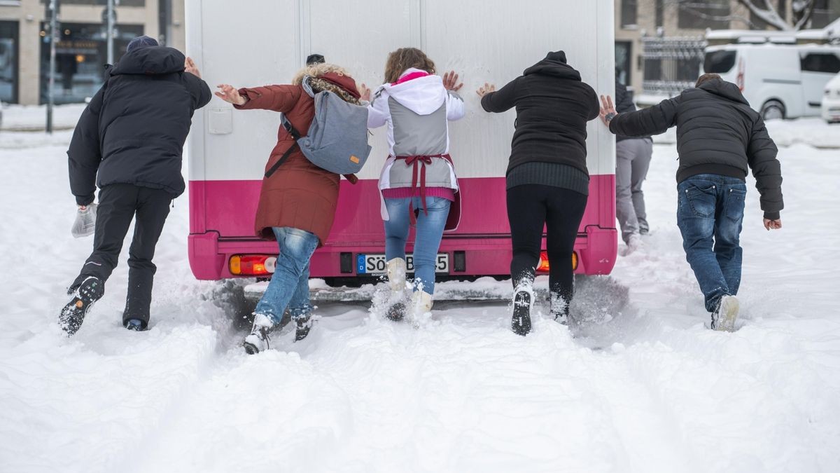 Helfer schieben am Nachmittag das Fahrzeug eines Verkaufsstandes auf dem Domplatz an (im Foto).