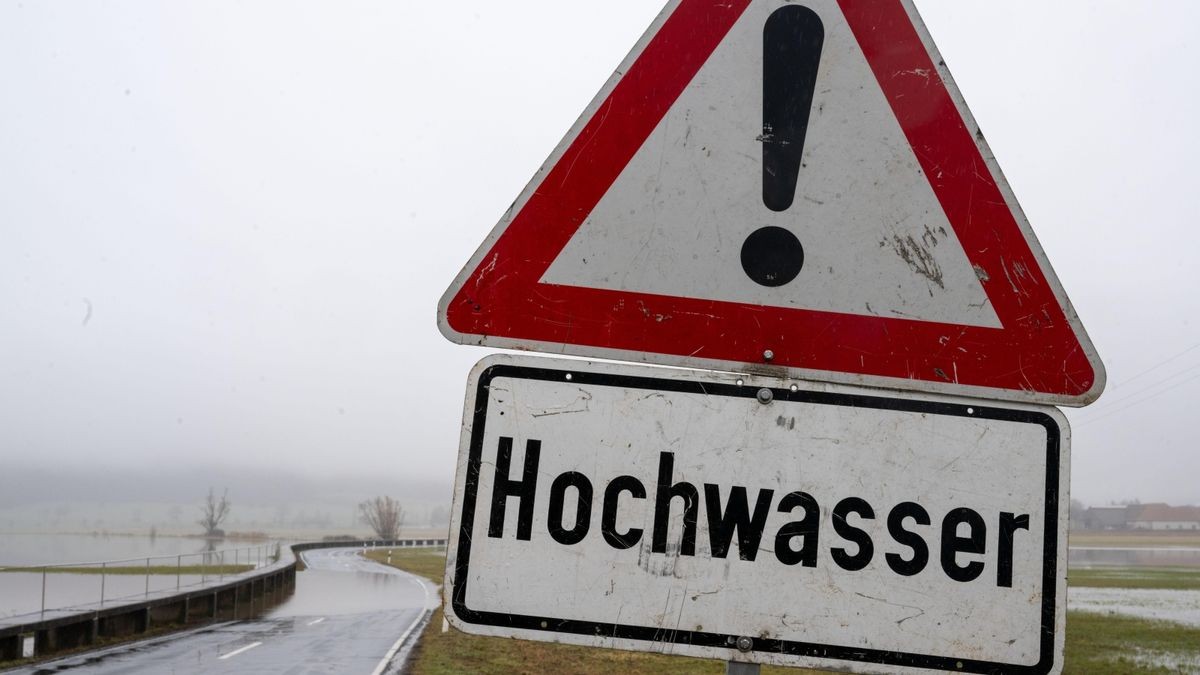 Ein Schild warnt vor Hochwasser, die Straße dahinter ist bereits zum Teil überschwemmt.