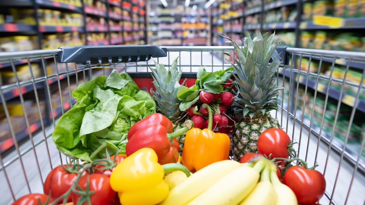 Ein Einkaufskorb mit Obst und Gemüse steht in einem Supermarkt.