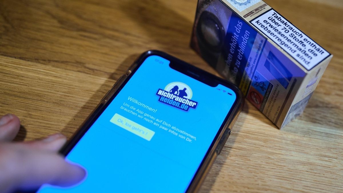 „NichtraucherHelden“ heißt eine App, die auf dem Bildschirm eines Mobiltelefons zu sehen ist. Dahinter liegt eine Schachtel Zigaretten. Ärzte in Deutschland können seit 2020 auch Gesundheits-Apps verschreiben.
