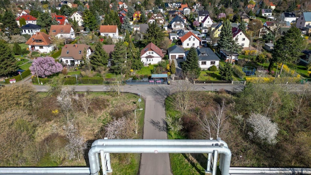 Eine Fernwärmeleitung führt neben einer Siedlung über eine Straße.