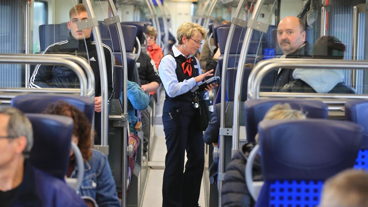 Eine Zugbegleiterin kontrolliert in einem Regionalzug die Fahrkarten der Reisenden. In den vergangenen Monaten hat die Zahl der Kriminalitätsdelikte im Schienennahverkehr zugenommen. Das Land und die Bahnunternehmen wollen deshalb Sicherheitsmaßnahmen verstärken (Symbolbild).