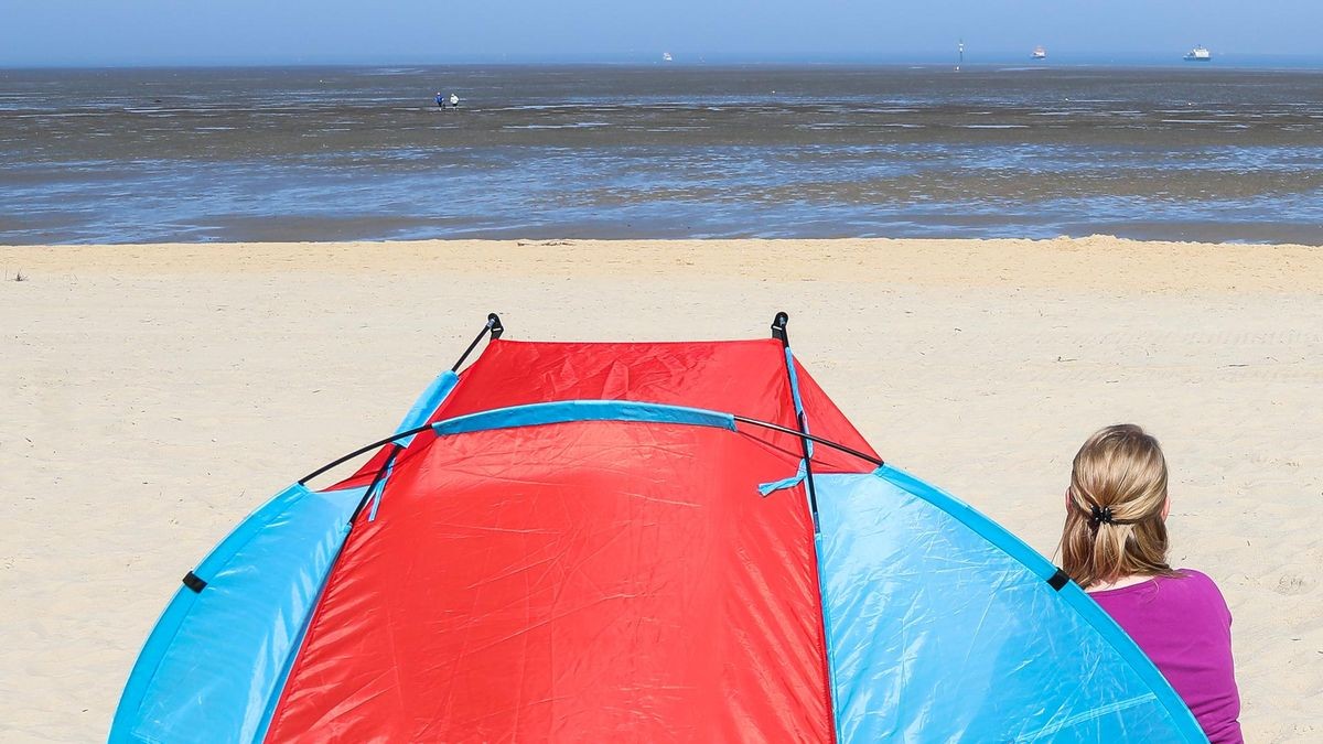 Eine Frau sitzt bei sommerlichem Wetter am Strand von Cuxhaven-Duhnen vor ihrer Strandmuschel.
