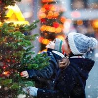 Zwei kleine Kinder, Jungen und Mädchen, die sich bei starkem Schneefall auf dem traditionellen Weihnachtsmarkt vergnügen. Glückliche Kinder genießen den traditionellen Familienmarkt in Deutschland. Zwillinge stehen am beleuchteten Weihnachtsbaum.