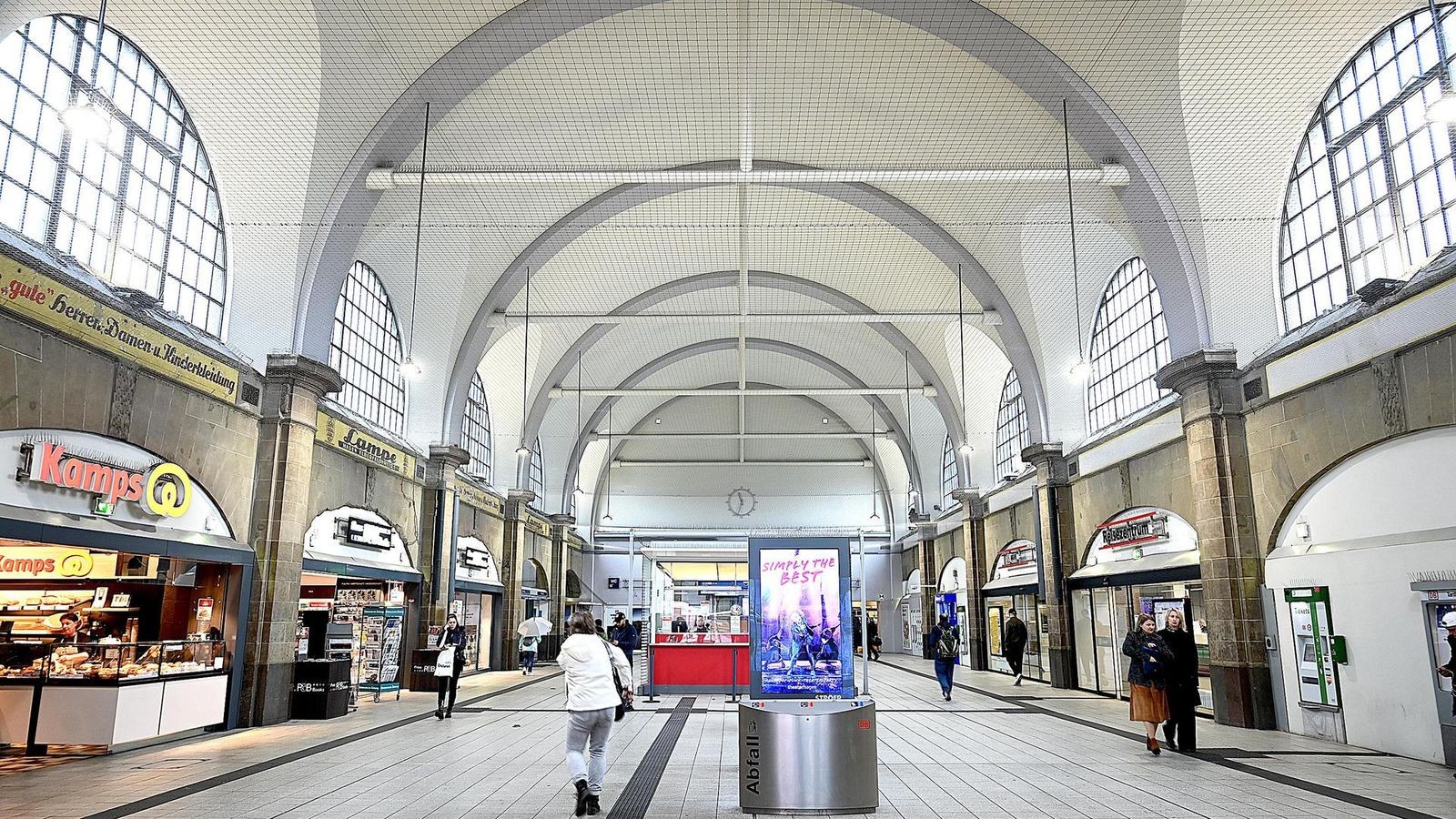 Frau-bel-stigt-Reisende-vor-Gesch-ft-in-der-Bahnhofshalle