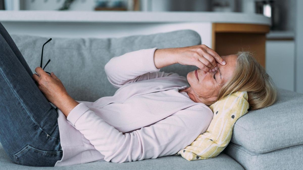 Eine Frau liegt mit sichtbaren Kopfschmerzen auf dem Sofa