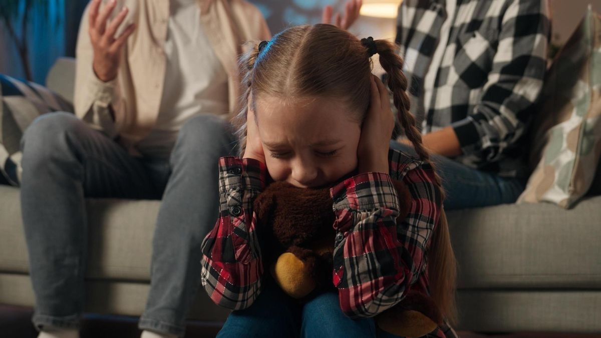 Sad child girl kid daughter upset suffering hugging toy Teddy bear close ears with hands ignore stress loud quarrel between parents mother father at home man woman arguments violence divorce family