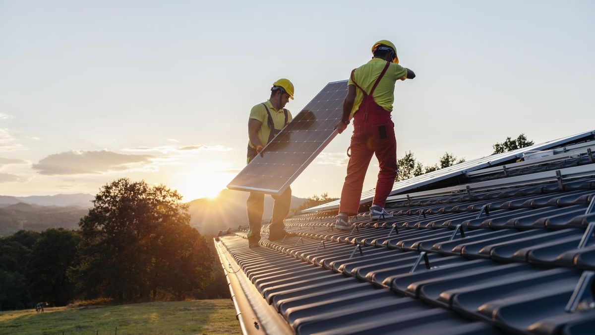 Workers Installing Solar Panels On Wooden House In Nature At Sunset.