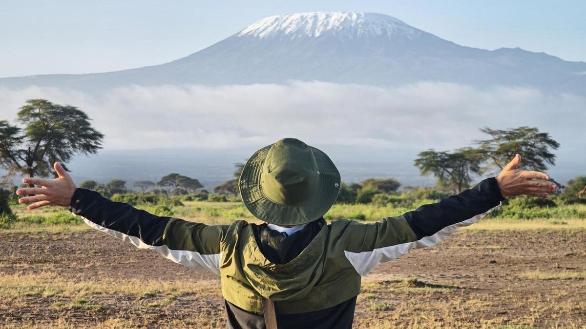 man walks against backdrop of Kilimanjaro. African walking safari. male traveler with backpack looking at amazing mountains. Hands to the side. travel concept, atmospheric moment