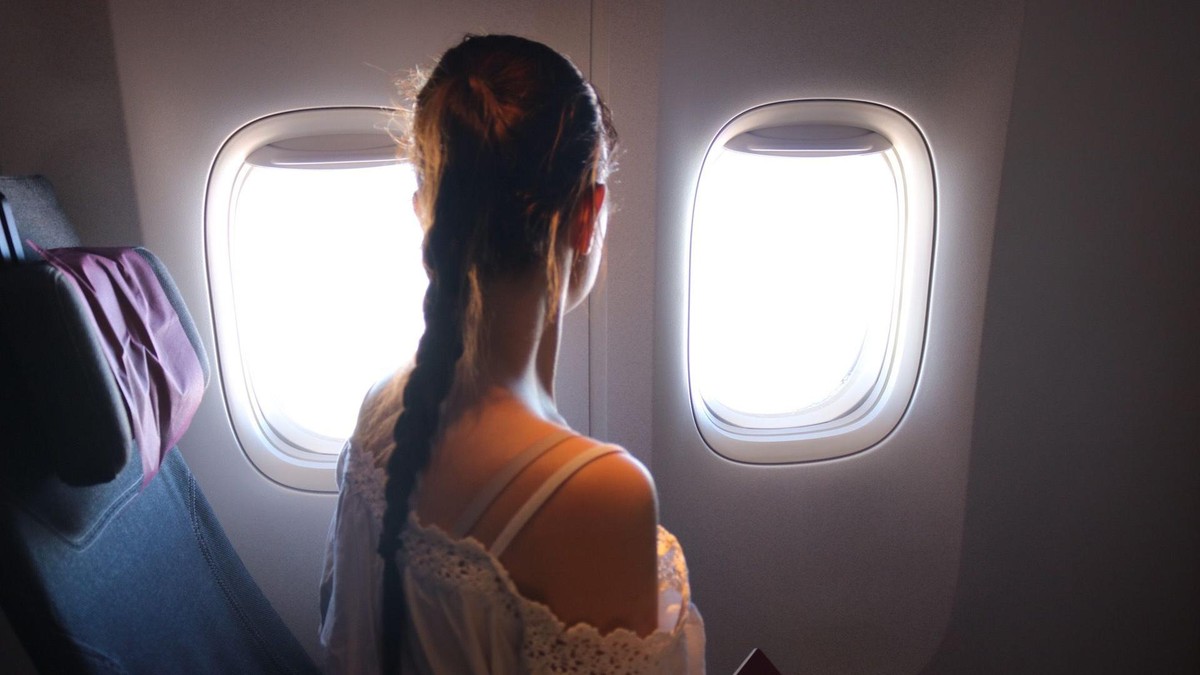 Jaqueline Schaupp sitzt auf einem Fensterplatz im Flugzeug und schaut aus dem Fenster, von hinten fotografiert.