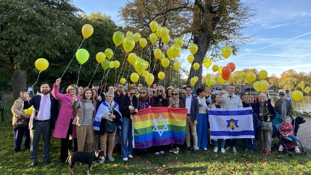Menschen an der Alster halten gelbe Luftballons und Israel-Fahnen hoch