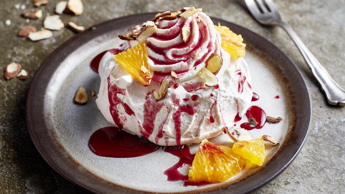 Teller mit weihnachtlicher Pavlova aus Lebkuchen, dazu Orangenstücke, Mandelblätter und Glühweinsirup