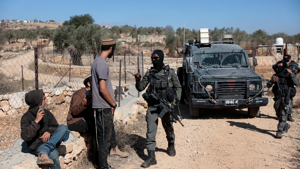 An Israeli border police officer holds back an Israeli settler trying to prevent Palestinians from harvesting olives, in Silwad